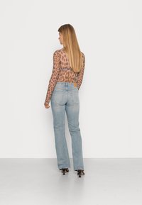 Top de manga longa em padrão leopardo marrom transparente, combinado com jeans claros de boca de sino. Saltos pretos de bico fino completam o visual. Acessórios mínimos.