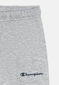 Sive trenirke od mekanog materijala, s elastičnim pojasom i malim mornarsko plavim "Champion" logotipom na donjoj lijevoj strani.
