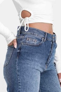 Jeans de mezclilla de tiro alto en un azul claro con una forma ajustada. Presentan un bolsillo trasero y un ligero desgaste. Se combinan con una parte superior blanca de canalé con cortes.