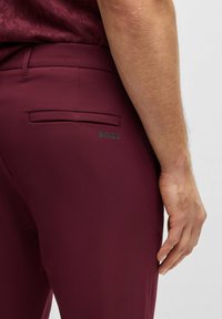 Burgundowe spodnie dopasowane z tylną kieszenią, subtelnym akcentem logo i gładką fakturą. Nowoczesny krój z czystymi liniami i detalami.