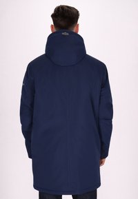 Parka blu navy con grande cappuccio, silhouette lunga, texture liscia e dettagli di cucitura sottili sulle maniche e sul retro.