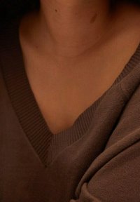 Brązowy sweter z dekoltem w serek wykonany z miękkiej dzianiny; cechuje się prążkowanym dekoltem i luźnym krojem, podkreślającym gładką teksturę.