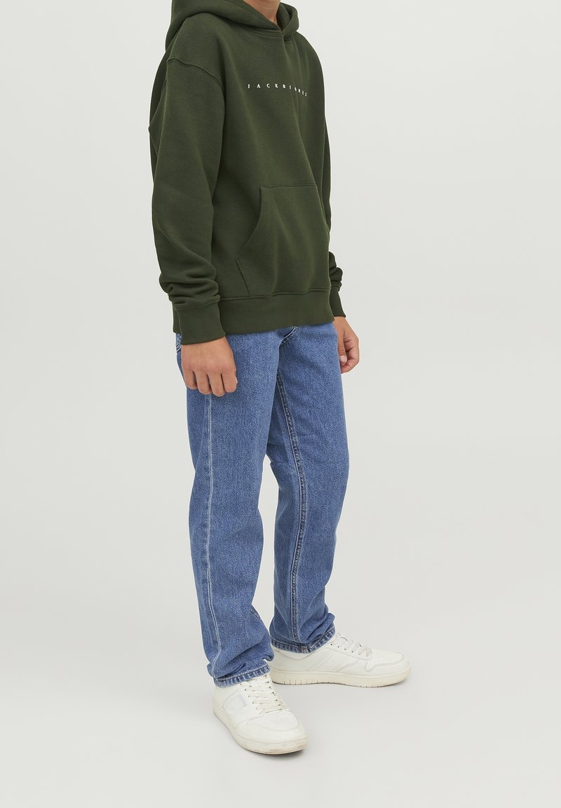 Grön hoodie med framficka och vit text, i kombination med blå denimjeans och vita sneakers. Enkelt design, avslappnad passform och avslappnad stil.