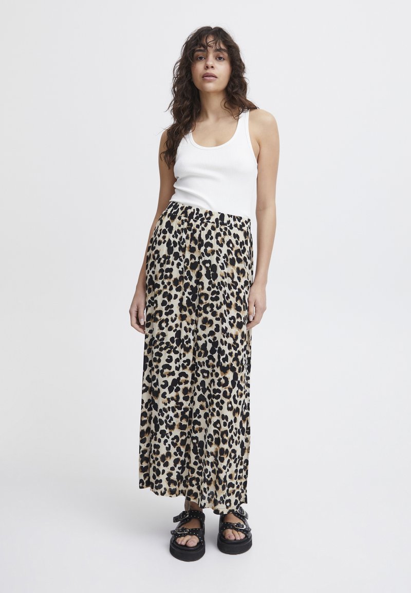 Beige Maxirock mit einem schwarz-braunen Leopardenmuster, aus leichtem Stoff. Kombiniert mit einem weißen, gerippten Tanktop und klobigen schwarzen Sandalen.