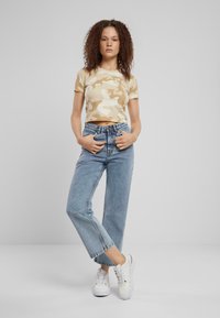 Camo-print avskåret t-skjorte i beige, kombinert med lyseblå høyhøydejeans og hvite sneakers med snøredetaljer.