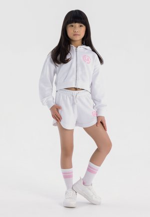Sudadera corta blanca con logo rosa, pantalones cortos blancos a juego, zapatillas blancas y calcetines blancos con rayas rosas, con un corte relajado y cordón.