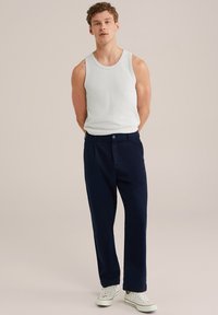 Witte geribbelde tanktop met marineblauwe recht gesneden broek en witte sneakers. De outfit heeft een eenvoudig, casual ontwerp zonder patronen.