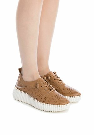 Sneaker in pelle marrone perforata con suola bianca scanalata, caratterizzati da un design con lacci e punta arrotondata, che evidenziano ventilazione e aderenza.