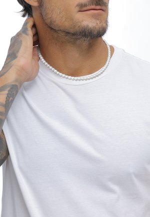 Hvid bomulds t-shirt med rund hals, parret med en snor af glatte, skinnende hvide perler omkring halsen. Hud med synlige tatoveringer.