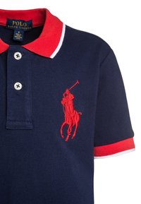 Mörkblå Polo Ralph Lauren-pikétröja med röd krage, vit kant och röd broderad polo-spelare logo på bröstet.