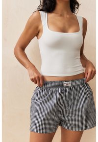 Débardeur blanc côtelé associé à un short à carreaux vichy bleu marine et blanc, doté d'une ceinture élastique et d'une étiquette à l'avant.