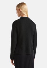 Černý pletený svetr s texturovanou vazbou, bez límce a s dlouhými rukávy, spárovaný s černou žebrovanou sukní.