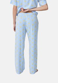 Pantaloni del pigiama blu chiaro con righe verticali e un motivo floreale di fiori gialli. Presentano una vita elastica e un taglio a gamba larga.