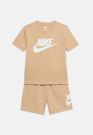 T-shirt Nike beige à manches courtes avec logo blanc et short beige assorti avec logo Nike blanc sur la jambe gauche.