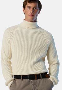 Maglione cream a coste con colletto alto realizzato in maglia testurizzata. Presenta maniche a raglan e un colletto aderente, abbinato a pantaloni grigi chiari e una cintura intrecciata.