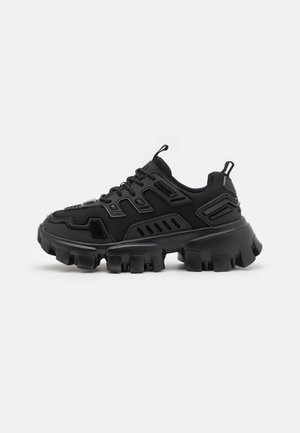 Sapato atlético preto com sola de borracha texturizada, elementos de design em camadas e detalhes reforçados. Inclui atacadores e uma alça no calcanhar.