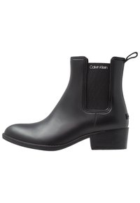 Des bottines noires présentent un extérieur en caoutchouc lisse, des panneaux latéraux élastiques, une pièce de traction et un petit talon carré pour plus de stabilité.