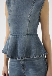 Top peplum in denim di un blu chiaro, con scollatura strutturata, orlo svasato e una leggera sfumatura. Abbinato a jeans coordinati per un look armonioso.