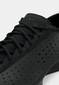 Gros plan d'une sneaker Nike Air noire avec des côtés perforés et des lacets noirs sur fond blanc.