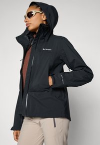 Black waterproof jacket with adjustable hood, front zipper, and ergonomic cuffs. Features Columbia logo and Omni-Tech detailing.