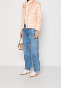 Jasnoróżowa pikowana kurtka z poziomym przeszyciem, w zestawieniu z niebieskimi jeansami o szerokich nogawkach i białymi trampkami z pomarańczowymi akcentami. Mała przezroczysta torebka.