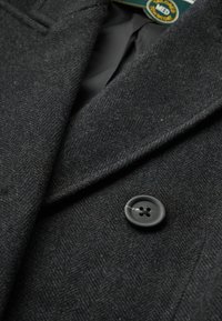 Dunkelgrauer Fischgrät-Mantelstoff mit glatter Textur. Er verfügt über einen auffälligen schwarzen Knopf mit vier Löchern und eine eingestickte Verzierung.
