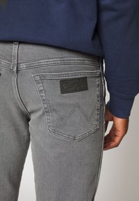 Grijze denim jeans met een aansluitend ontwerp, voorzien van een zwart leren label op de achterzak en subtiele stikselaccenten.