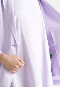 Lekki lniany blezer w jasnym lawendowym kolorze z pojedynczym zapięciem na guzik, przednią kieszenią oraz podszewką z dopasowanego materiału dla spójnego wyglądu.