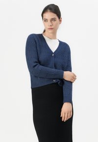 Navy ribbed knit cardigan with a v-neck and long sleeves, featuring a single heart-shaped button closure and cropped hemline.