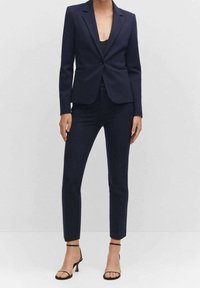 Granatowa marynarka dopasowana, z długimi rękawami, jednolitym zapięciem na guzik, w połączeniu ze spodniami slim-fit i czarnymi sandałami na obcasie. Gładka tekstura materiału.