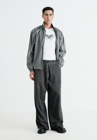 Gray athletic jacket with white accents, white t-shirt featuring a graphic, patterned loose black pants, and chunky black shoes.