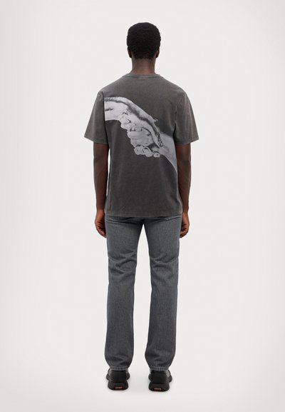 T-shirt gris à manches courtes avec un grand graphique en noir et blanc d'une main au dos. Associé à un jean droit gris foncé.