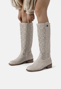 Stivali al ginocchio grigio chiaro con design floreale perforato, materiale superiore morbido e tacco basso impilato. Presenta dettagli con bottoni sul lato.