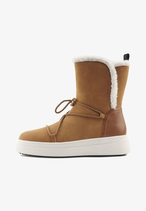 Brune ruskind ankelstøvle med hvid kunstpelsforing og hvid gummisål. Har snøre detaljer til justering og brune læderdetaljer.