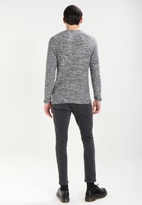 Un pull gris à manches longues avec un motif texturé, associé à un jean slim gris foncé et des chaussures noires à lacets. Vue de l'arrière.