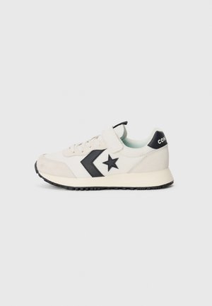Hvid lavtop sneaker med sort stjerne-logo, snørebånd og velcro-strop, beige ruskindsdetaljer og sort gummisål på grå baggrund.