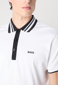 White polo shirt with a black striped collar, three black buttons, and a small "BOSS" logo on the left chest area. Smooth texture.