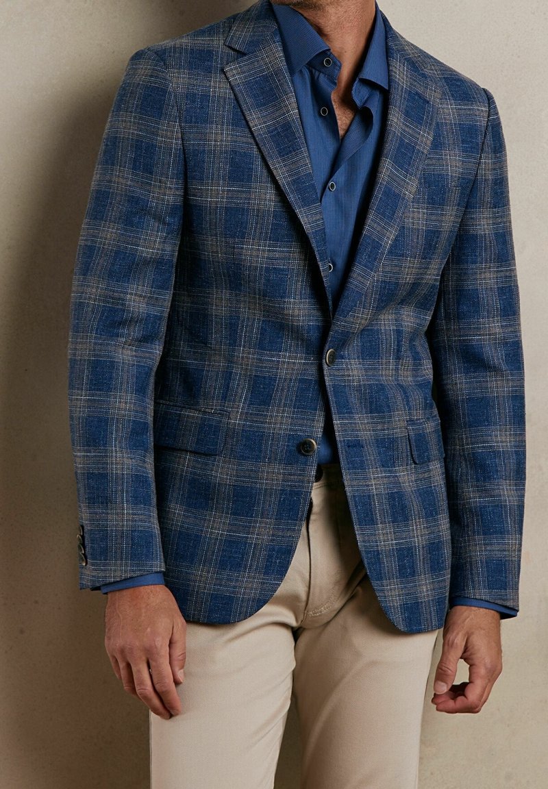 Blå rutigt kavaj med en texturerad tyg, med ljusgrå linjer, två framfickor och en enkel knapplåsning. Kombineras med en blå skjorta.