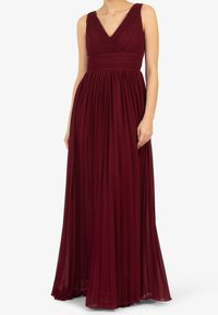 Lång bordeauxklänning med V-ringning, plisserad liv och flödande kjol. Tillverkad av lätt material med breda remmar och insvängd midja.
