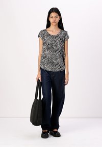 Top de manga corta con estampado en blanco y negro combinado con jeans de pierna ancha en azul oscuro, llevando un bolso tote negro; textura de tela suave.