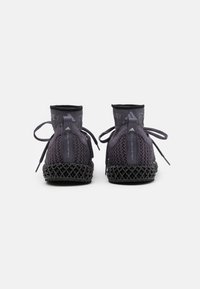 Černé pletené tenisky s vysokým, elastickým otvorem podobným ponožce, s texturovaným šněrováním vpředu a charakteristickou mřížkovou mezipodešví.