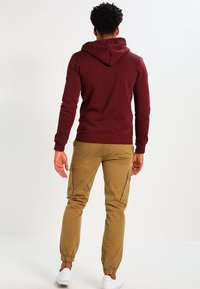 Sudadera burdeos con cordón y bolsillo tipo canguro, combinada con pantalones cargo beige que tienen bolsillos laterales y puños elásticos. Zapatillas blancas.