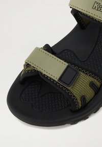 Črne in olivno zelene sandale s teksturiranim podplatom, nastavljivim trakom s črno kovino in ojačanim šivanjem v športnem slogu.