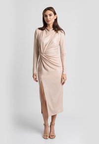 Dopasowana, różowo-złota sukienka z długim rękawem, z twisted front design, rozcięciem do kolan i gładką strukturą. Uzupełniona beżowymi paskami na kostkę.