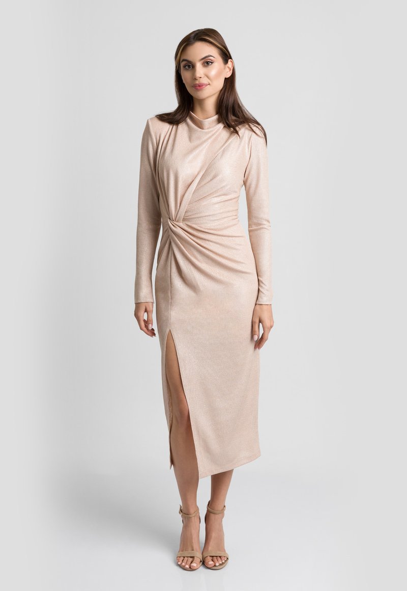 Dopasowana, różowo-złota sukienka z długim rękawem, z twisted front design, rozcięciem do kolan i gładką strukturą. Uzupełniona beżowymi paskami na kostkę.