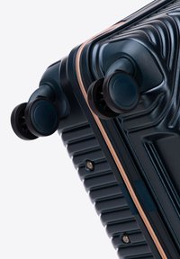 Valigia rigida di colore blu navy con texture a righe, zip in rame e doppie ruote nere per la mobilità. Caratterizzata da un design resistente e accenti prominenti.