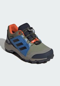 Zielono-niebieski but na zewnątrz z teksturowaną cholewką, czarnymi paskami, gumową podeszwą i systemem szybkiego sznurowania. Wnętrze z pomarańczowymi akcentami.
