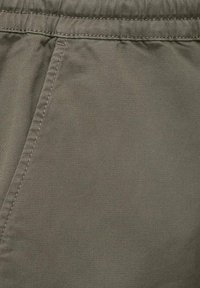 Närbild av en grågrön tygficka med synliga sömmar och ett rynkat midjeband på ett plagg.