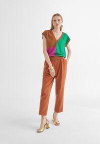 Kolorowy dziany top w brązowe, zielone i różowe panele; w połączeniu z spodniami w kolorze rdzy i złotymi sandałami na obcasie.