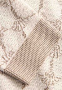 Tela de suéter de punto beige claro con un patrón floral en beige más oscuro, con textura de puño acanalado de color beige sólido.